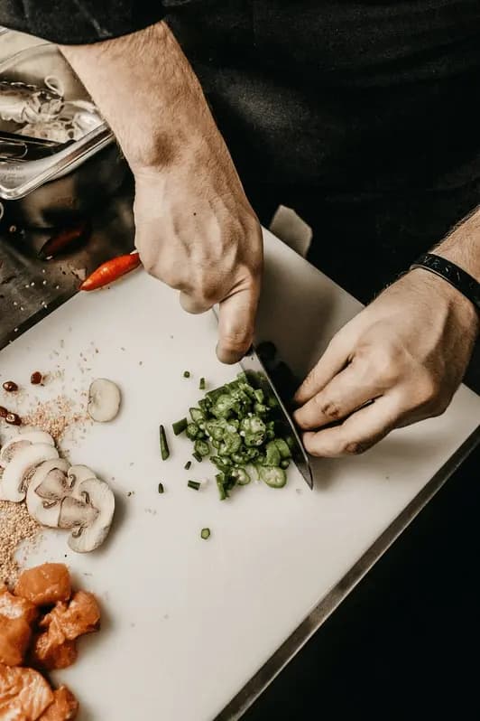 Skärbräda ovanifrån med två vita händer som hackar grön chili